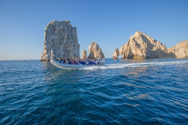 A group in a tour boat in front of the Arch of Cabo San Lucas