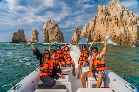 A tour group posing in a boat in front of the Arch of Cabo San Lucas