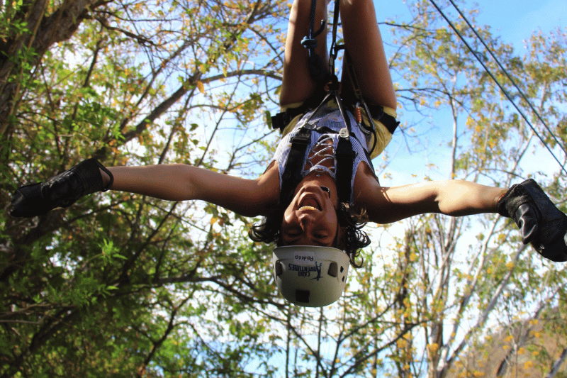 woman upside down on a zipline wearing the proper safety equipment